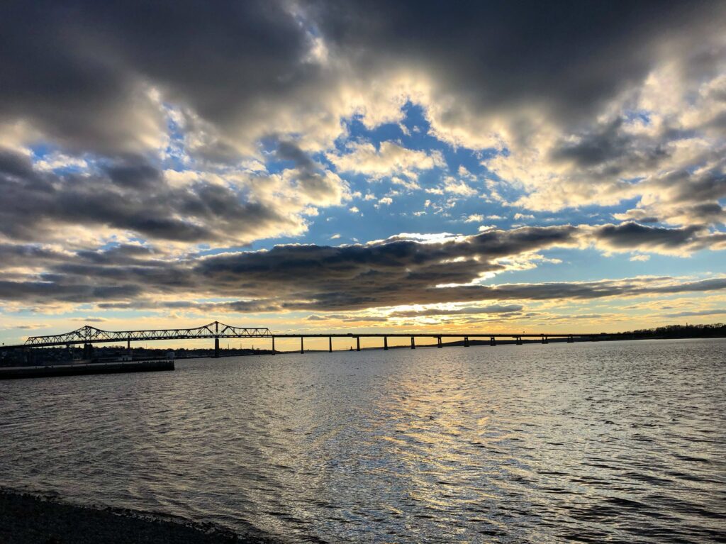 a sunset with a bridge extending across a large river